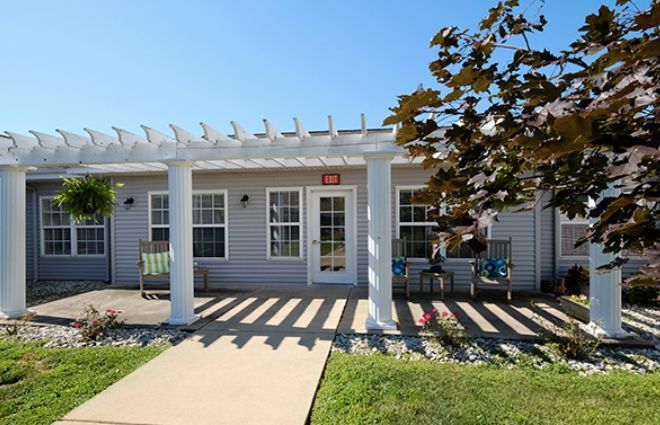 A cozy house with a pergola-covered patio and a well-maintained front yard under a clear blue sky.