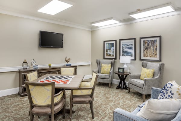 A cozy living room area with seating and a table for games, featuring wall-mounted artwork and a television.