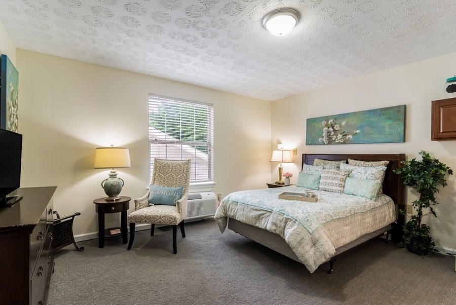 A cozy bedroom with a bed, two lamps, a chair, and a window.