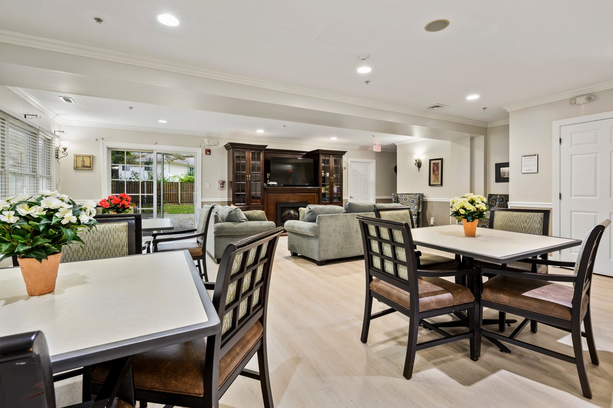 A spacious and well-lit living area featuring comfortable seating, a television, bookshelves, and dining tables.