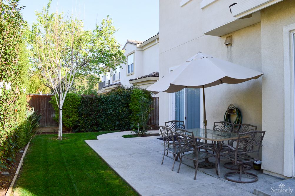 A well-maintained backyard with a patio featuring outdoor furniture and a large umbrella, surrounded by a lush green lawn and trees.