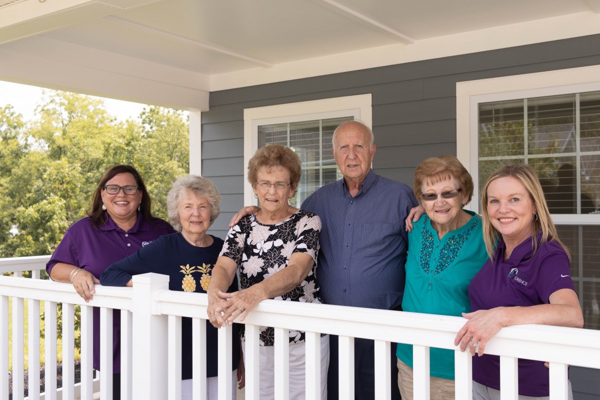 A group of people posing together on a porch, smiling at the camera.