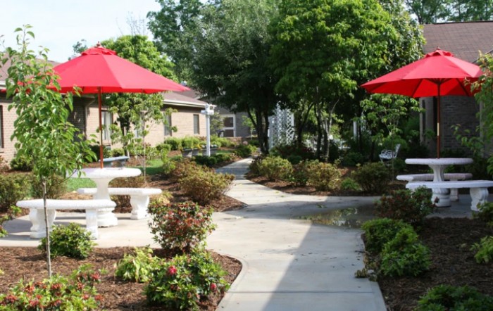 A scenic garden with a winding pathway and outdoor seating under red umbrellas.