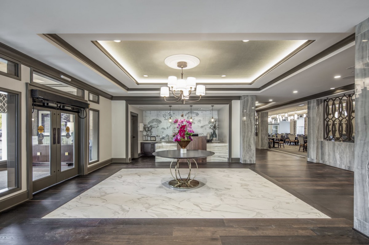 A modern lobby with elegant interior design, featuring a chandelier and a table with flowers on marble flooring.