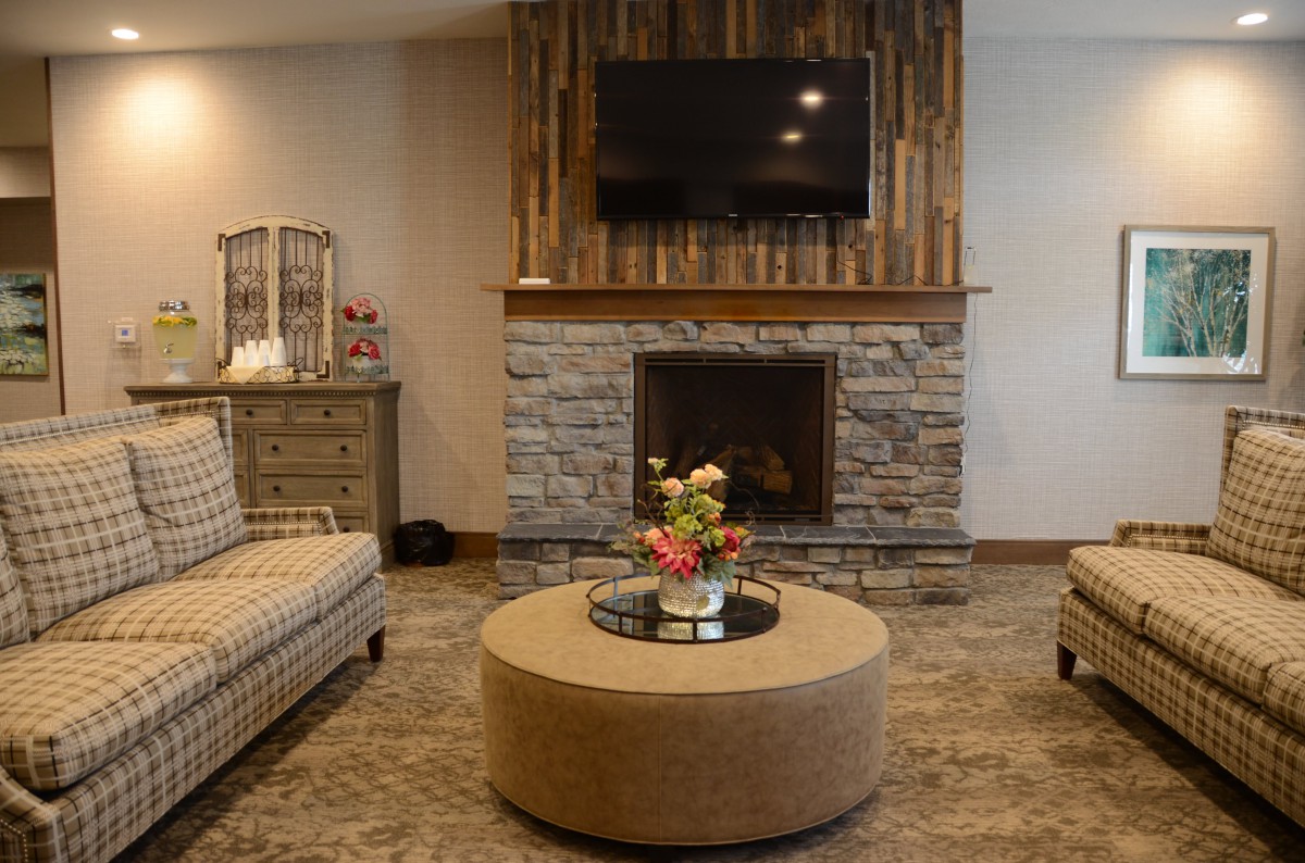 A cozy living room featuring a stone fireplace and wood-paneled wall, with comfortable seating and a round coffee table.