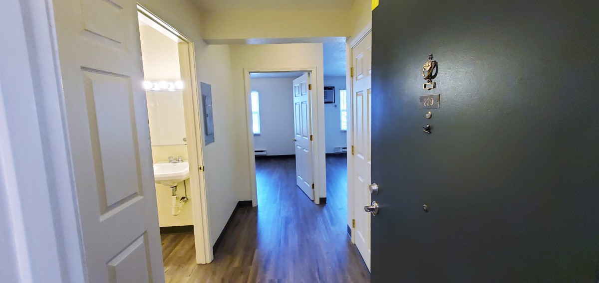 View of an apartment hallway from the entrance with doors leading to different rooms.