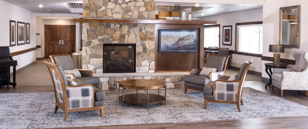 A cozy living room features a stone fireplace, modern armchairs, and a stylish coffee table on a patterned rug.