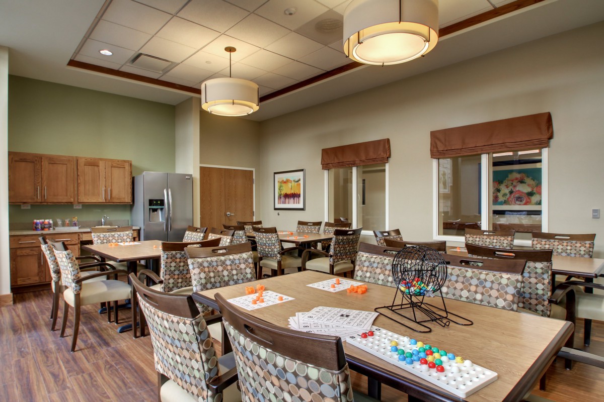 A modern dining room with neatly arranged tables and chairs, contemporary lighting fixtures, and an adjoining kitchen area.