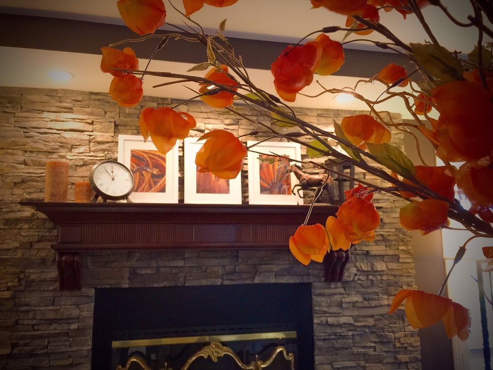 A cozy fireplace mantel decorated with autumn leaves and a clock.