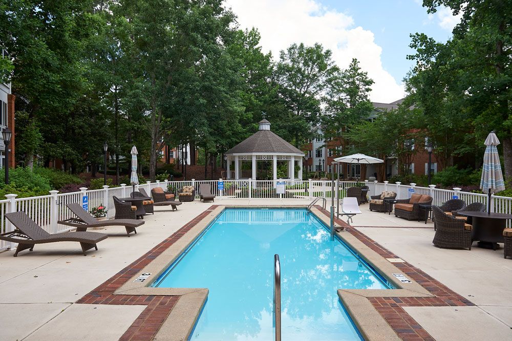 Outdoor swimming pool area with lounge chairs and a gazebo surrounded by trees.
