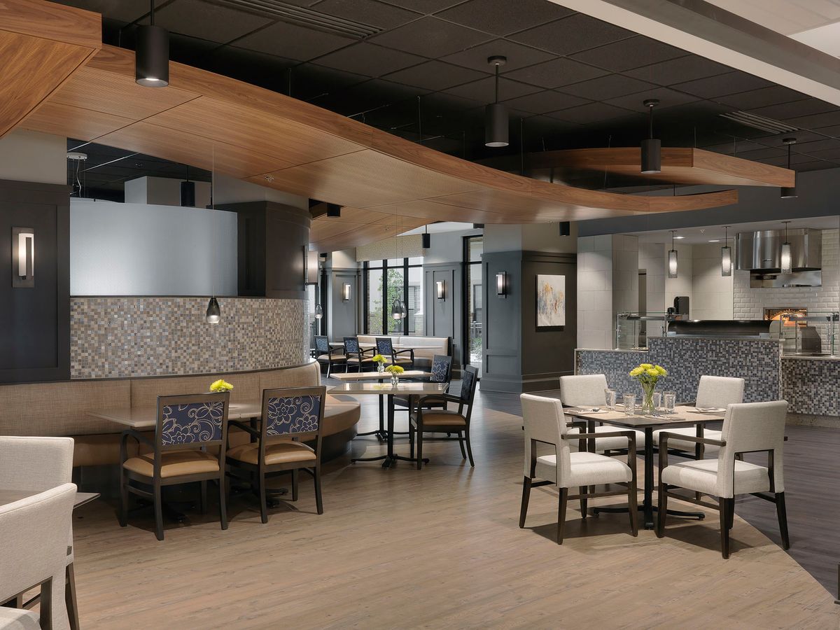 A modern restaurant interior with neatly arranged tables and chairs, featuring a stylish ceiling and wooden flooring.