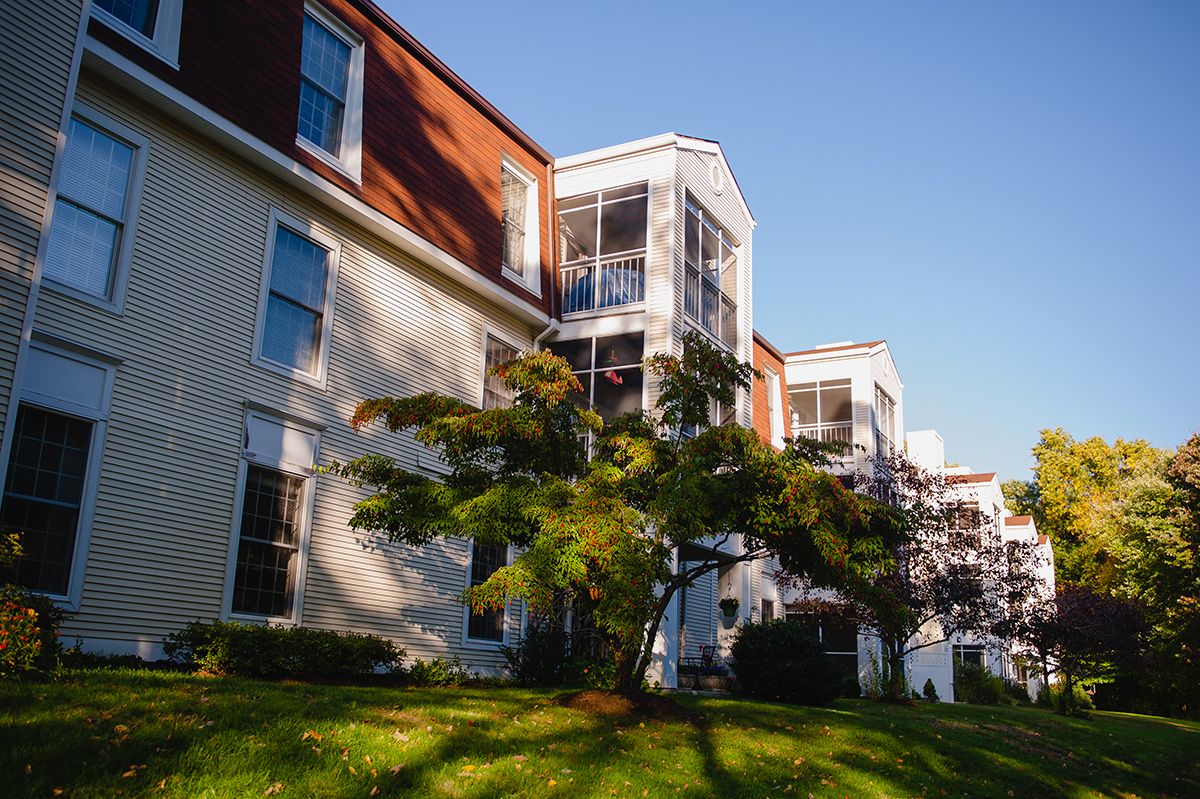 A residential building with red and beige exteriors, surrounded by greenery and illuminated by sunlight.