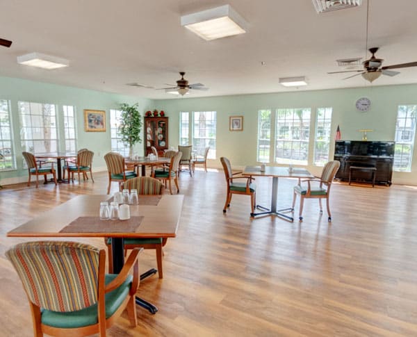 A spacious and bright dining area with multiple tables and chairs, featuring large windows and a wooden floor.