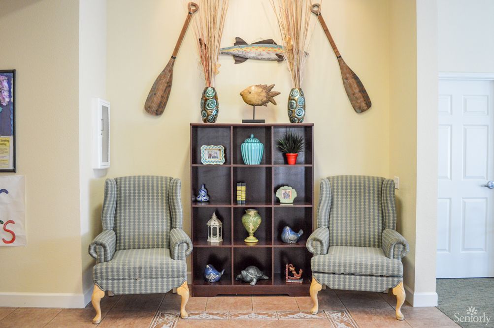 A cozy living room setup with two armchairs, a decorative shelf, and wall-mounted oars.