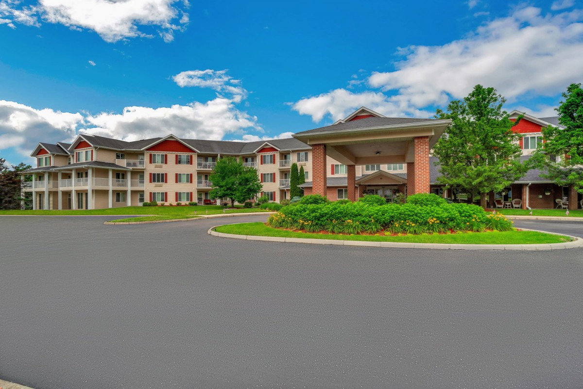 A large, multi-story residential building surrounded by greenery and a clear blue sky.