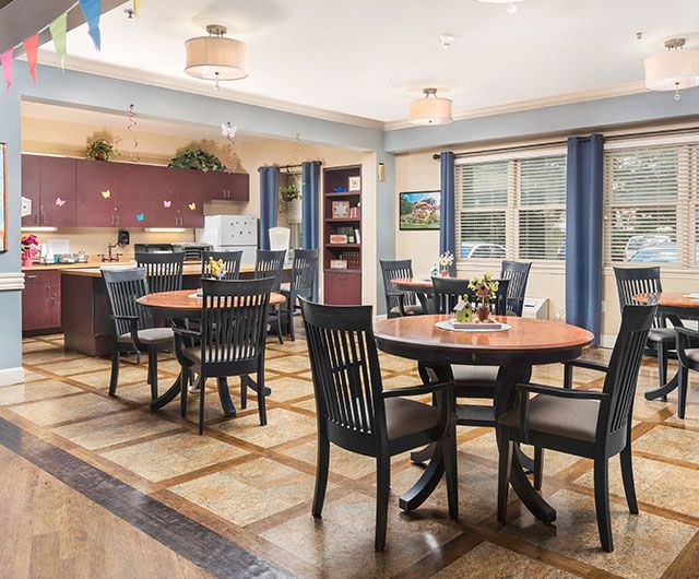 A spacious dining area with round tables and chairs, featuring a kitchen space in the background.