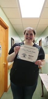 A person smiling while holding a certificate in a hallway.