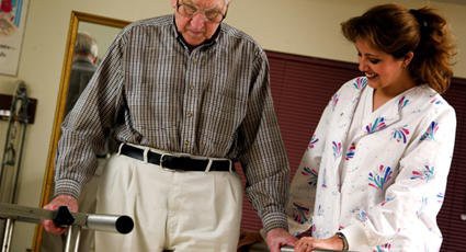 An elderly person receiving support with a walking aid.