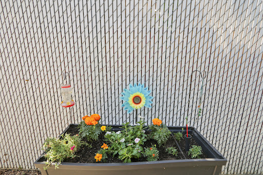 A vibrant raised garden bed filled with colorful flowers and a decorative flower stake against a textured wall.