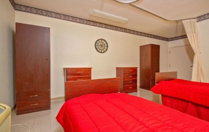 A tidy bedroom featuring twin beds with red bedding, wooden dressers, a wardrobe, and a wall clock.