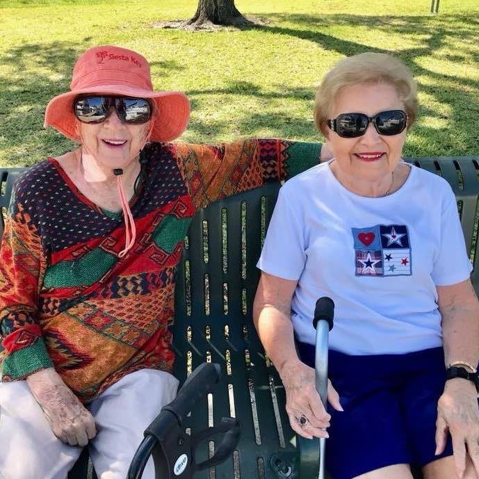 Two elderly women sitting on a bench in the park, enjoying the sunny day.