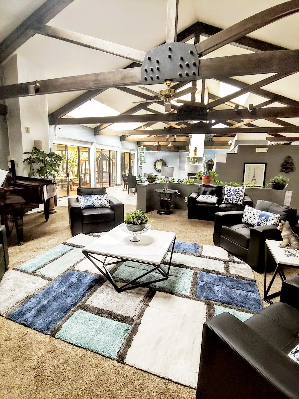 A spacious and modern living room featuring exposed wooden beams, a grand piano, and stylish furniture.