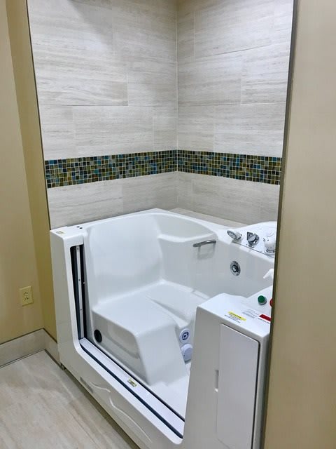 An accessible walk-in bathtub with a built-in seat in a tiled bathroom.