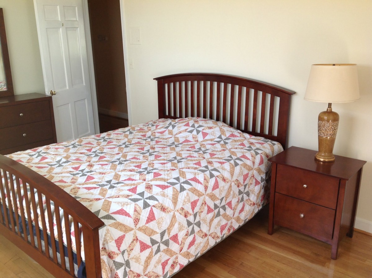 A cozy bedroom featuring a wooden bed with a colorful quilt and a matching nightstand with a lamp.