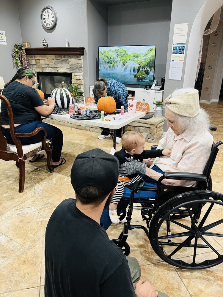 A family gathering where an elderly woman in a wheelchair interacts with a child in a cozy living room adorned with autumn decorations.