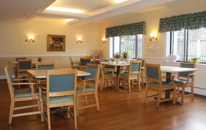 A cozy dining area with several tables and chairs, featuring wooden flooring and natural lighting from the windows.