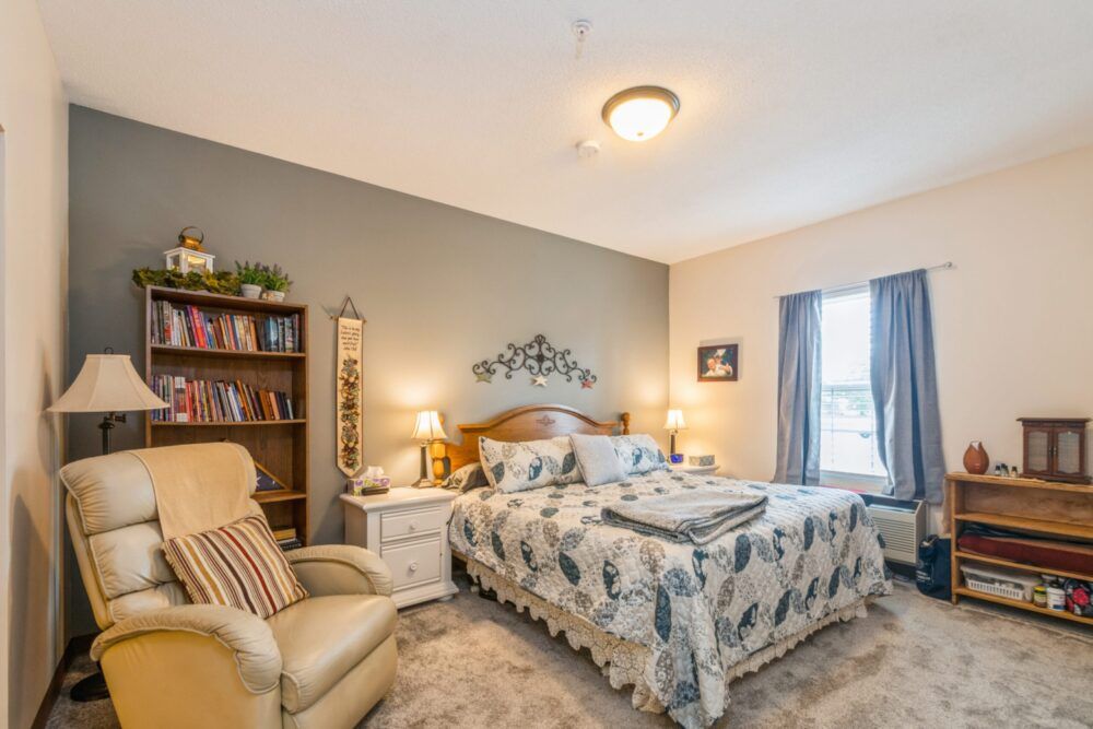 A cozy, well-decorated bedroom with a comfortable bed, armchair, and bookshelf.