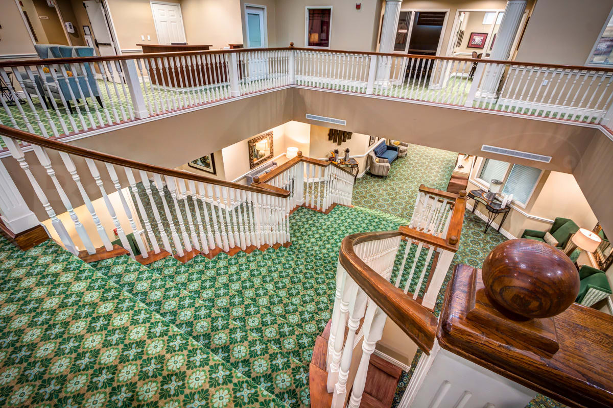 A well-lit interior featuring a carpeted staircase and balcony area with wooden railings.