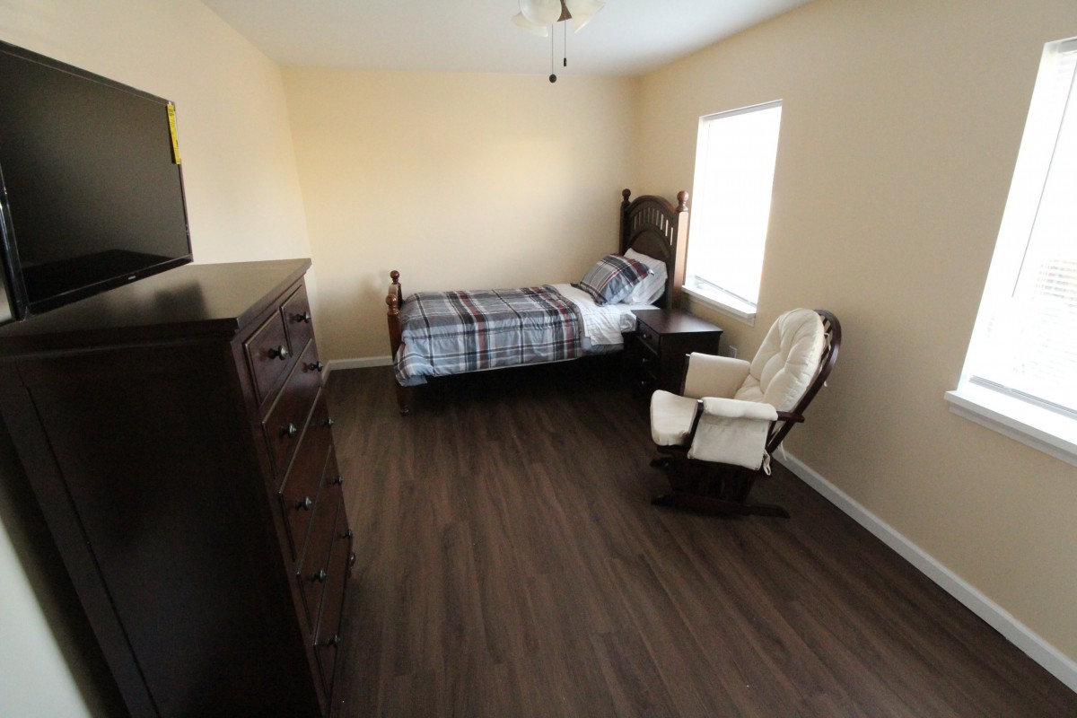 A simple bedroom with a single bed, dresser, and rocking chair.