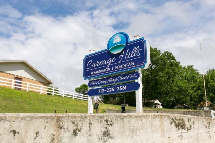 An outdoor sign for Carriage Hills Rehabilitation & Healthcare, featuring contact information and set against a grassy landscape.