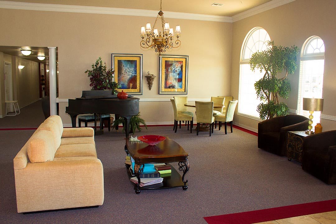 A cozy living room with elegant decor, featuring a piano, chandelier, and dining area.