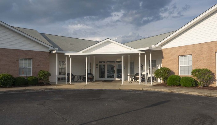 A building with a covered entrance and white columns under a cloudy sky.