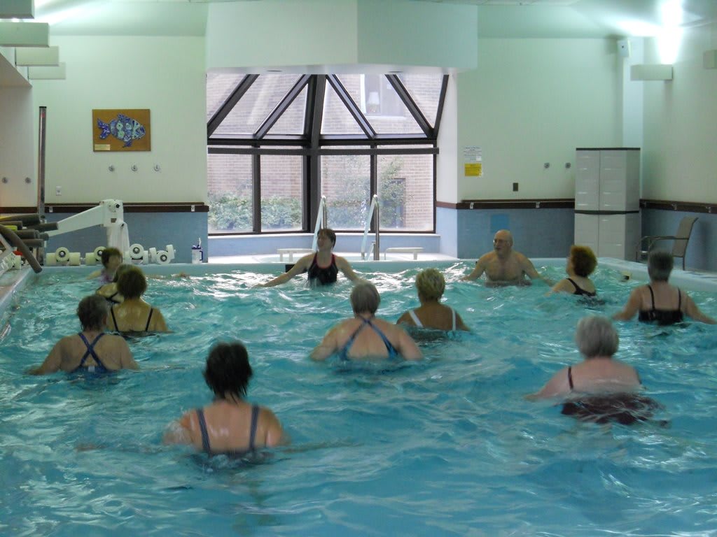 A group of people participating in a water aerobics class at an indoor swimming pool.