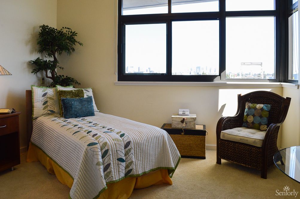 A modern bedroom with a single bed, cozy chair, and large window allowing natural light.