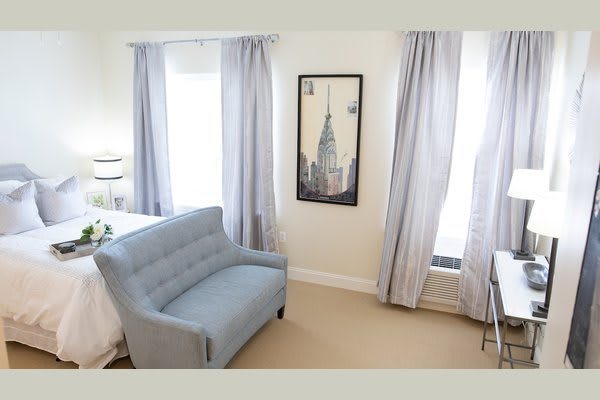 A cozy living room featuring a blue sofa, light curtains, and artwork on the wall.