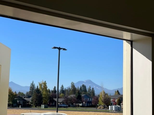 View of a mountain landscape through a window, with houses and trees in the foreground.