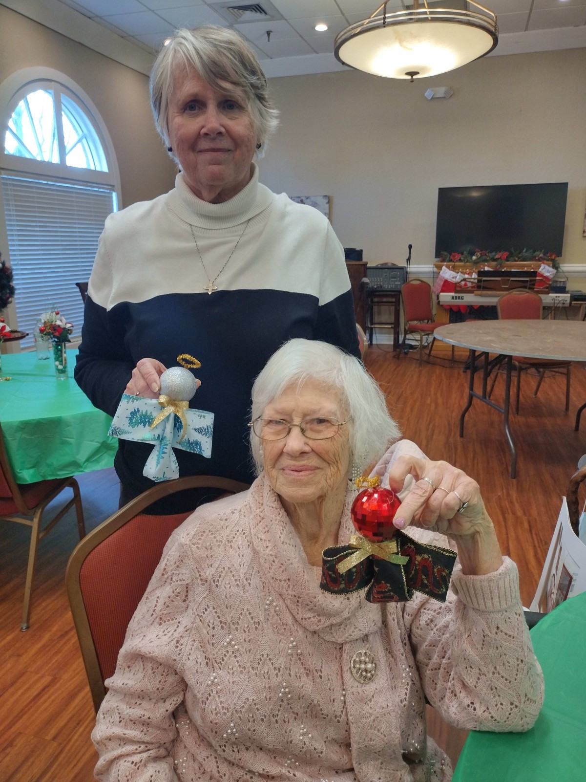 Two women at a social gathering holding handmade crafts.