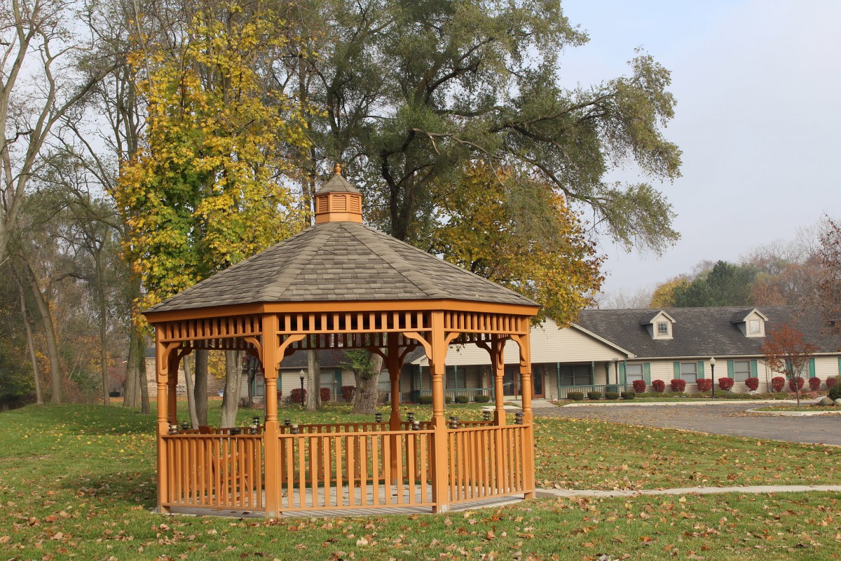 A wooden gazebo in a park surrounded by autumn trees.