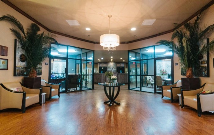 A modern lobby with a chandelier, glass doors, and a central table surrounded by seating.