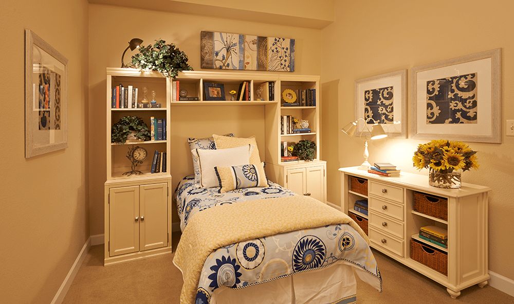 A cozy bedroom with a single bed, bookshelf, and warm lighting.