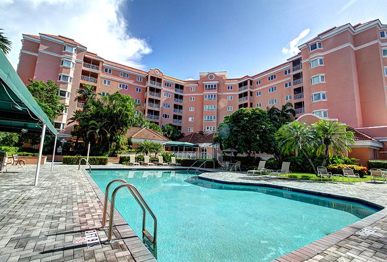 A scenic view of a residential apartment complex with a clear blue swimming pool under a bright sky.