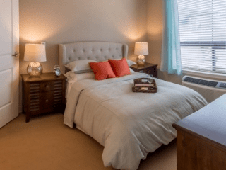 A cozy bedroom with a neatly made bed adorned with orange pillows, flanked by wooden nightstands and warm lighting from table lamps.