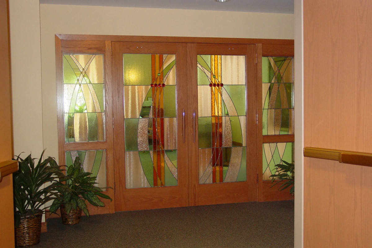 A set of stained glass doors with a wooden frame, decorated with plants on either side.