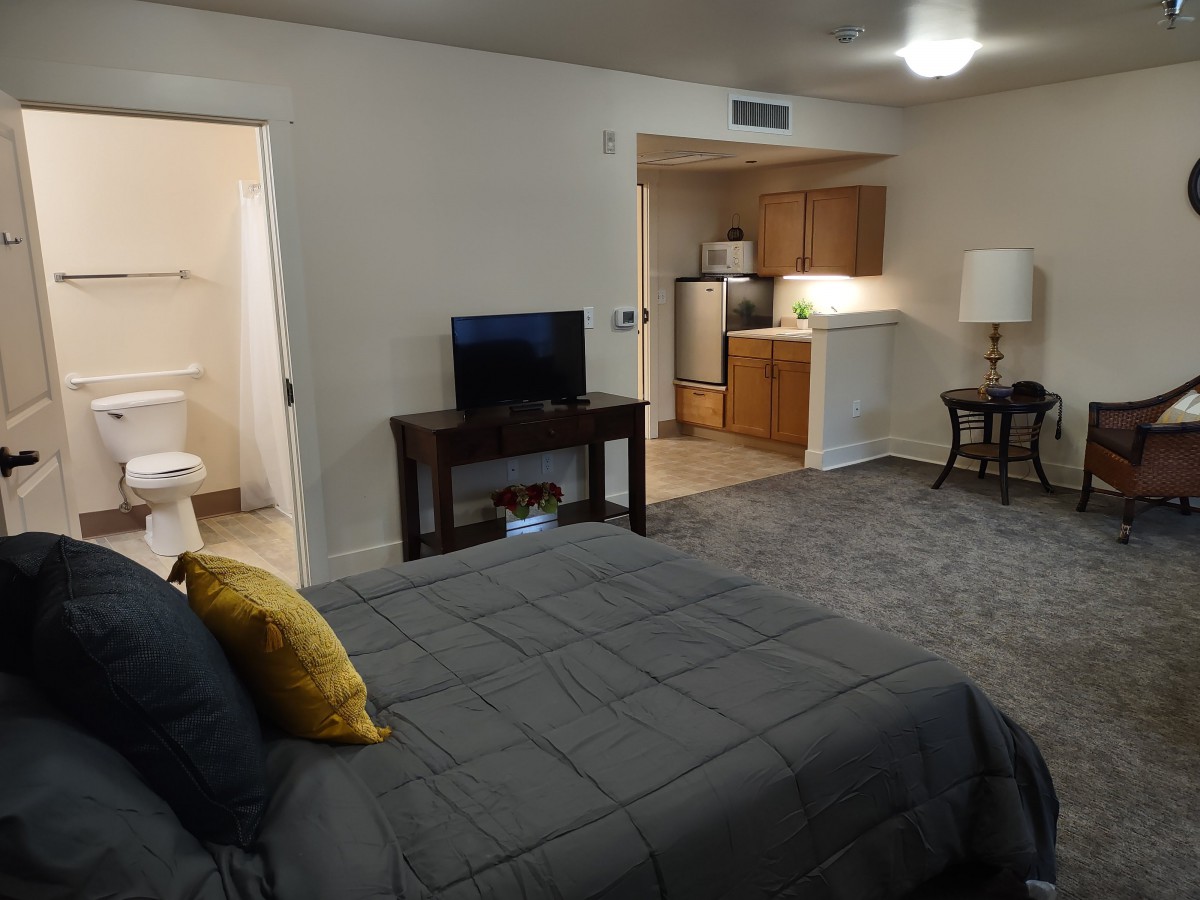 A cozy apartment bedroom with a kitchenette and TV.