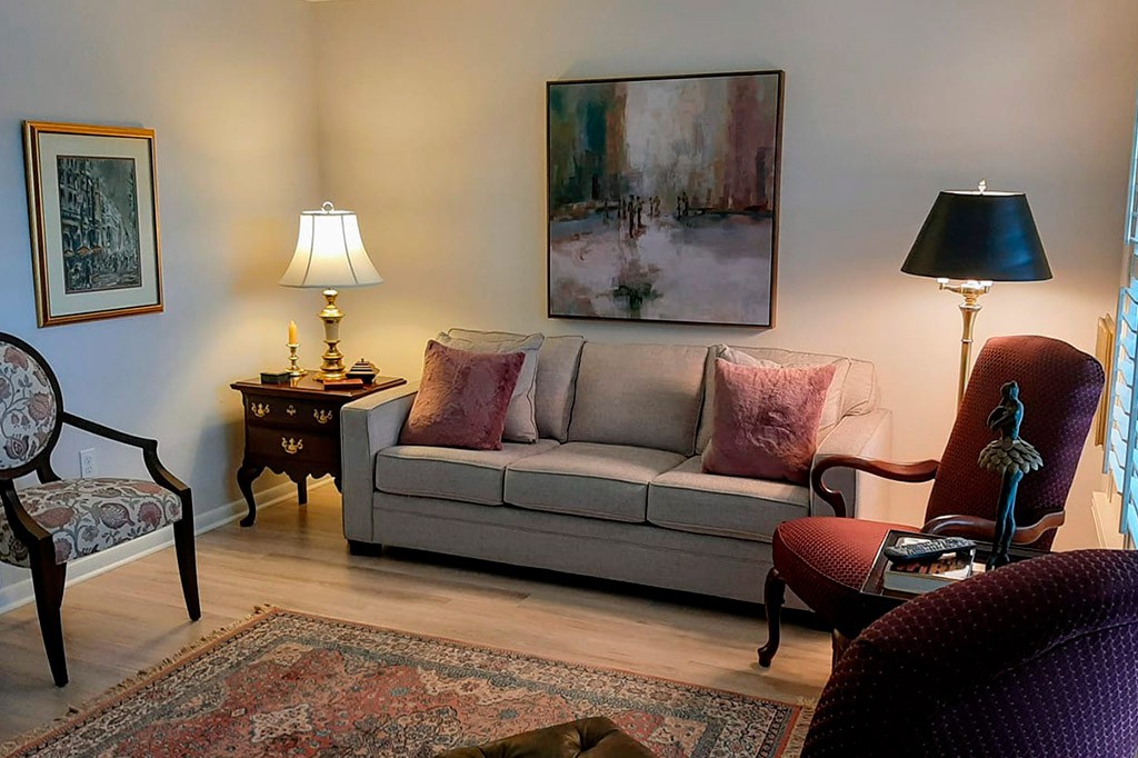 A cozy living room featuring a comfortable sofa with cushions, an elegant lamp on a side table, and abstract artwork on the wall.