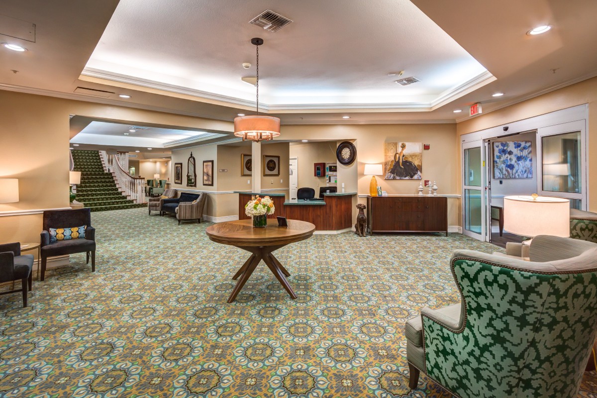 A well-lit hotel lobby with elegant decor, featuring a central table and reception desk.
